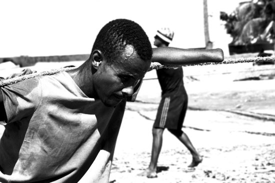 Fotografía documental blanco y negro primer plano pescador sin una mano tirando de cuerda pesada, expresión de esfuerzo, costa colombiana