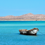Fotografía artística de una lancha de pescador vieja en aguas turquesas del mar Caribe en La Guajira, Colombia, con un paisaje costero árido al fondo.