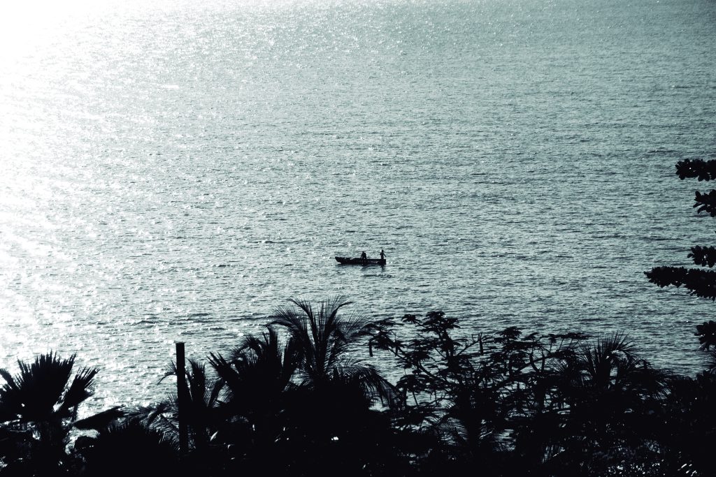 Fotografía artística blanco y negro pescadores bote contraluz mar brillante, palmeras silueta, costa tropical.