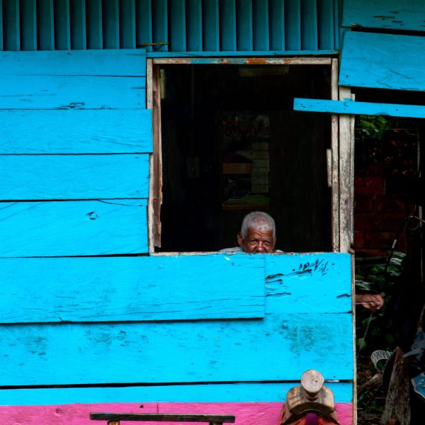 Fotografía artística hombre anciano tejedor asomado ventana casa madera azul y rosa, silla de montar exterior, vida rural