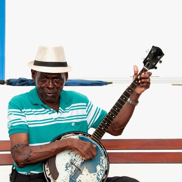 Fotografía artística músico panameño tocando banjo desgastado con sombrero, interpretando son cubano, sentado en banco