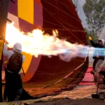 trabajador usando llama para inflar globo aerostático en espacio industrial