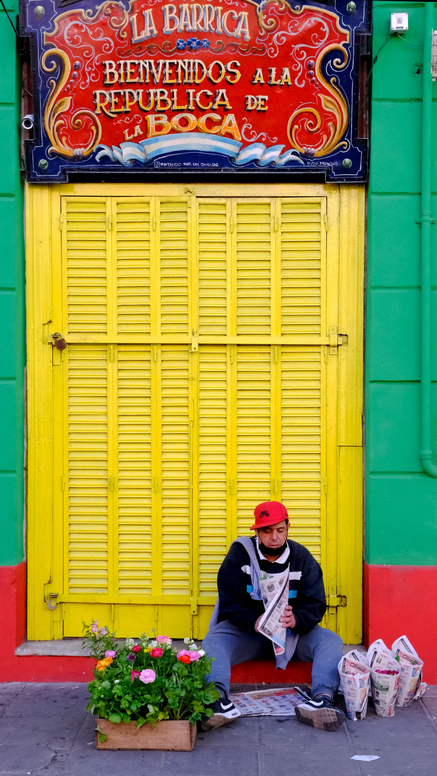 hombre sentado organizando flores frente a fachada colorida
